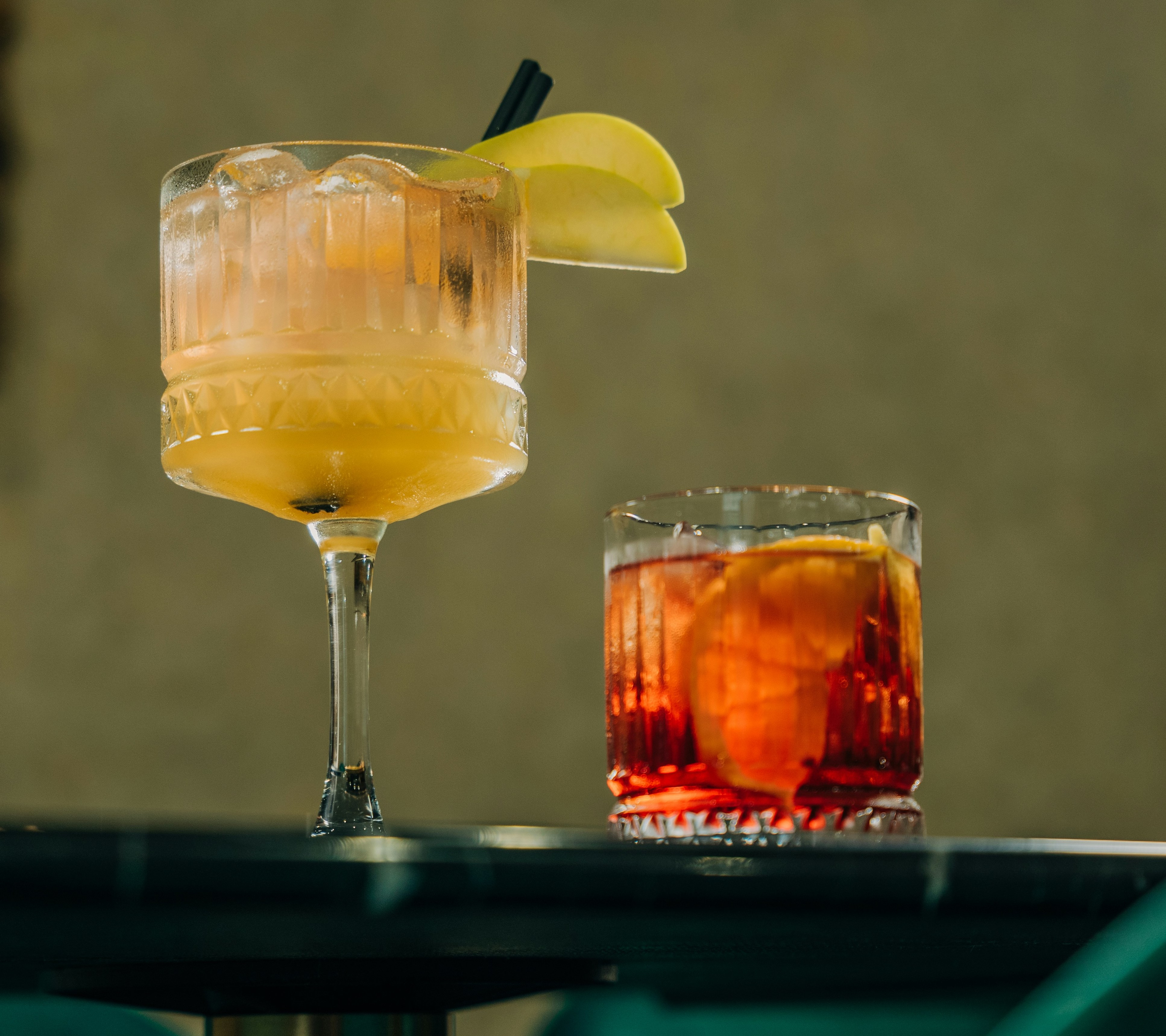2 classic sugar shot cocktails on a bar counter, one is a tall yellow drink and the other is red/brown drink in a wiskey glass, both with a lemon garnish