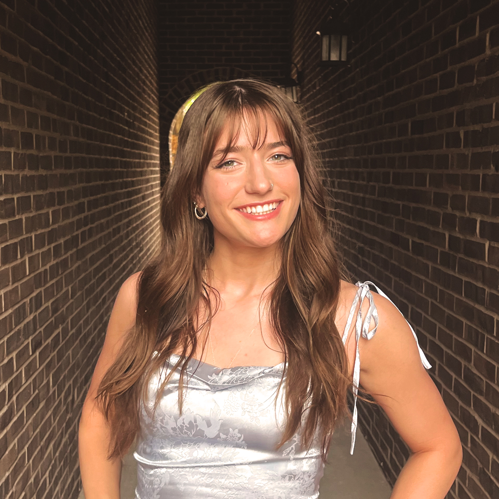 profile picture of myself wearing a blue dress infront of a dark brick background
